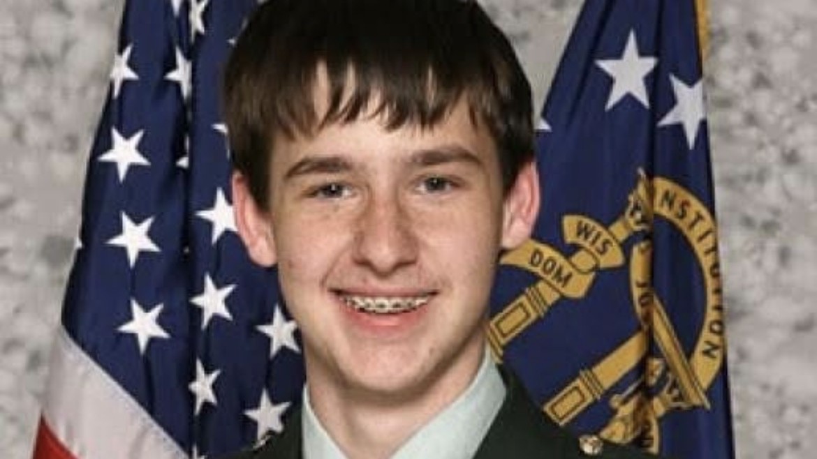 Tyler Long smiling in his JROTC dress uniform, in front of American and state flags